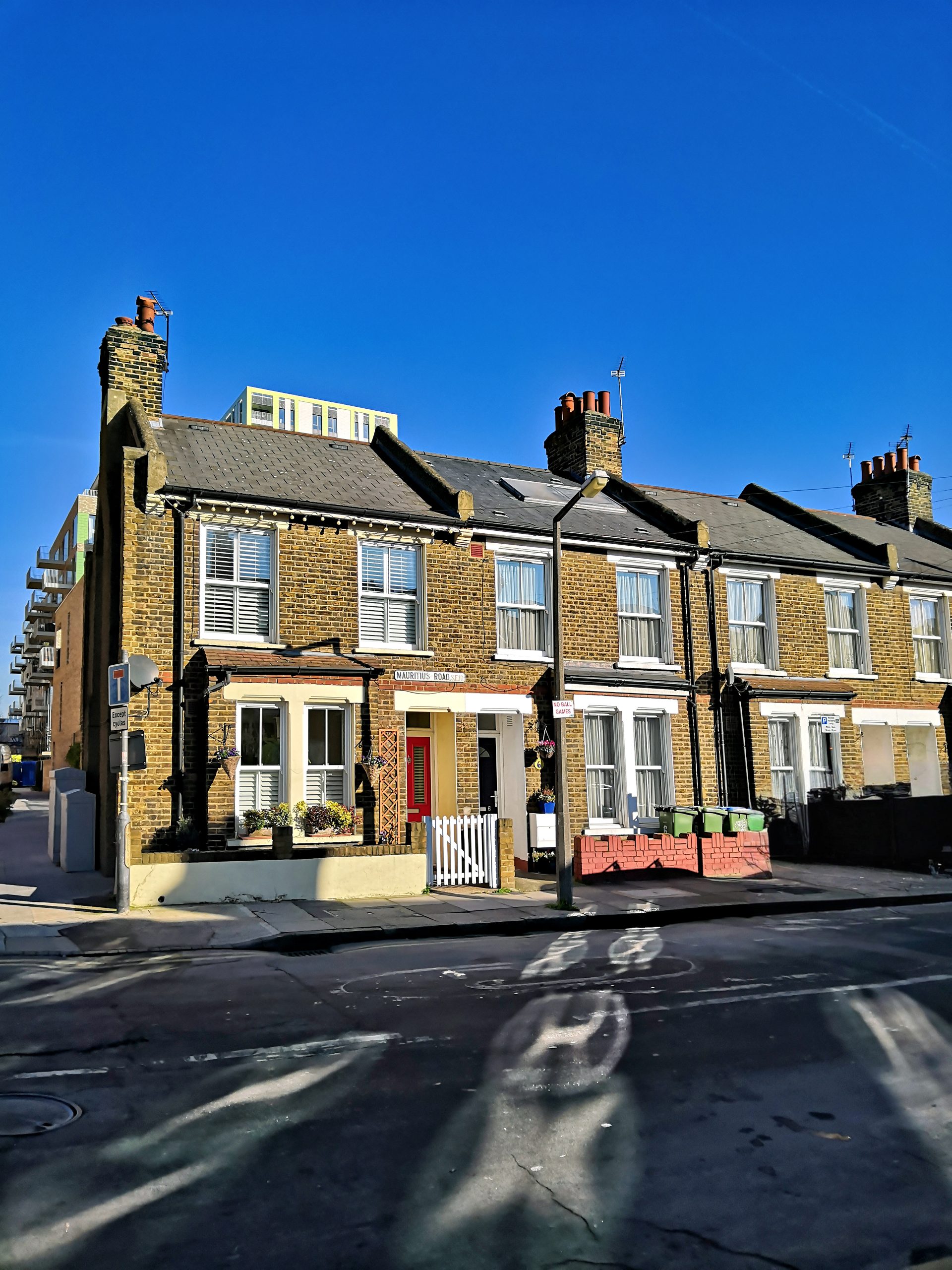 A row of brick terraced houses with chimneys under a clear blue sky, featuring a bright red door and white picket fence in front, reminiscent of the charming environments you might find showcased in an API Playground.