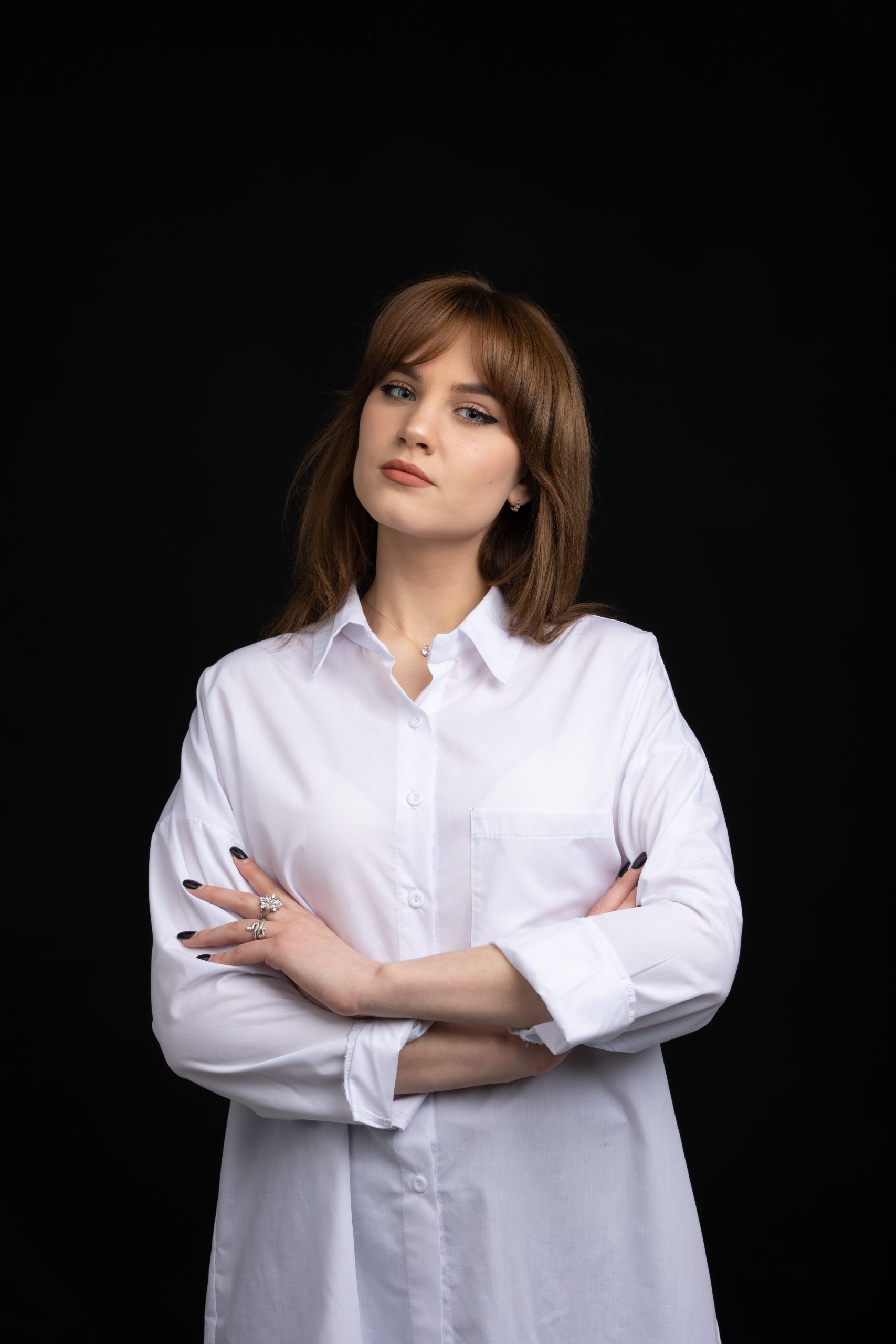 A woman with light brown hair, wearing a white button-up shirt, stands against a black background with arms crossed and a serious expression, embodying the professional style often featured in img.ly visuals.