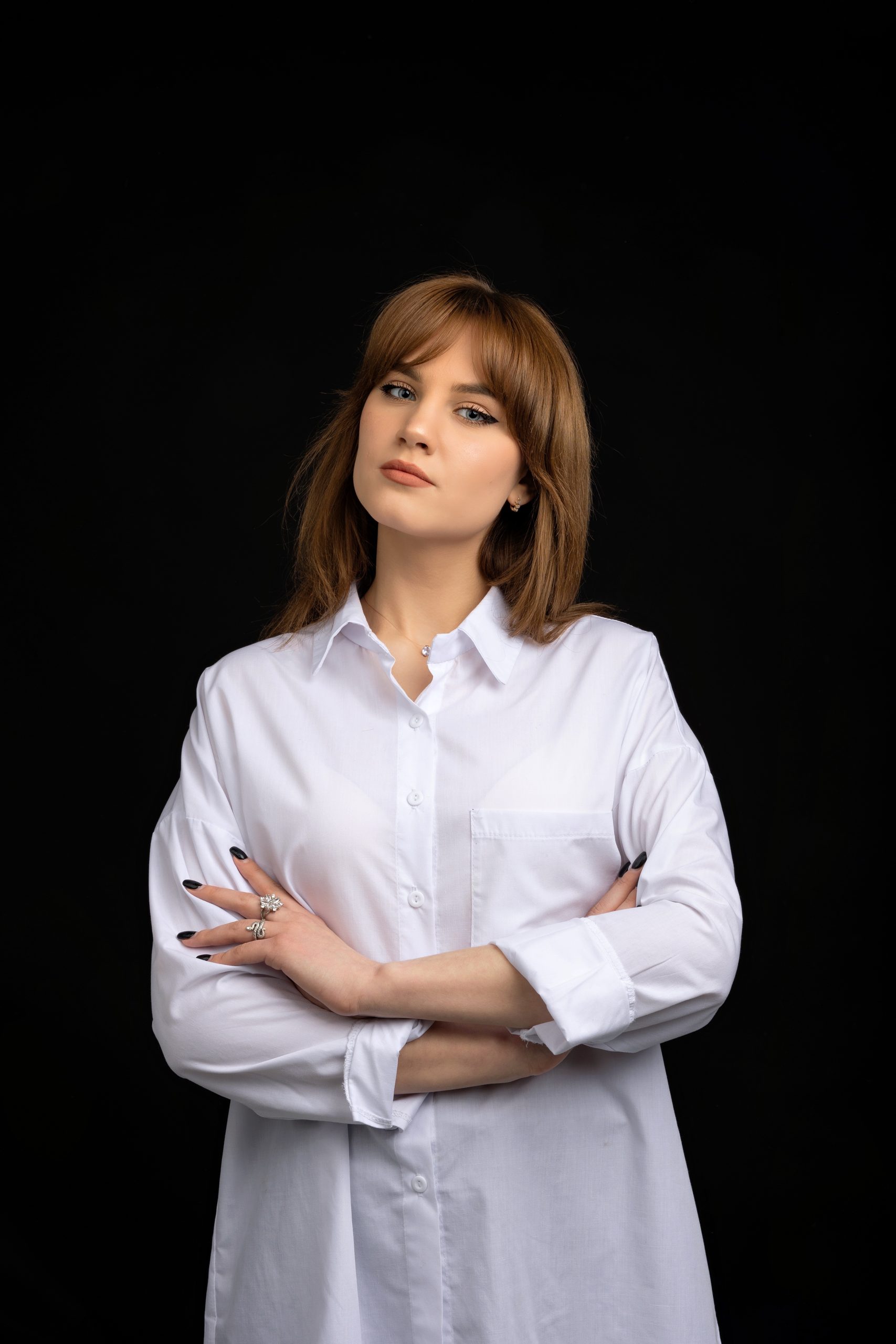 A woman with light brown hair wearing a white button-up shirt stands against a black background with her arms folded, looking confidently at the camera, as if ready for an img.ly portrait session.